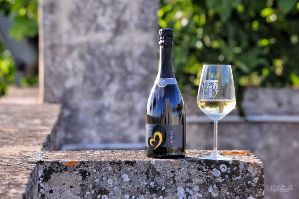 Wine bottle and glass of white wine on a stone step outdoors on a sunny day.