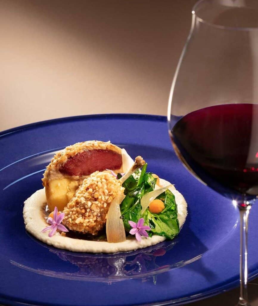 Gourmet meal on a blue plate accompanied by a glass of red wine.