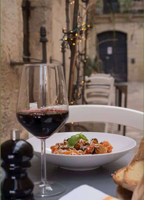 Red wine glass and bowl of pasta on a table at La Cucina Di Mamma Elvira in Lecce, Italy.