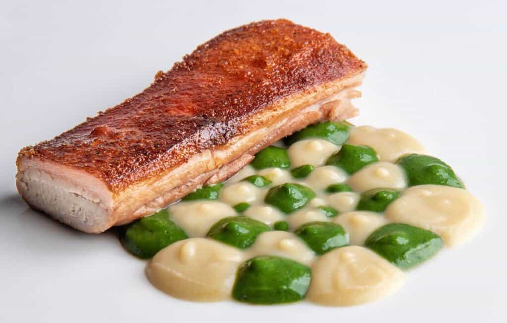 Gourmet dish of seared pork belly on a bed of pureed peas and potatoes at a restaurant in Lecce, Italy.